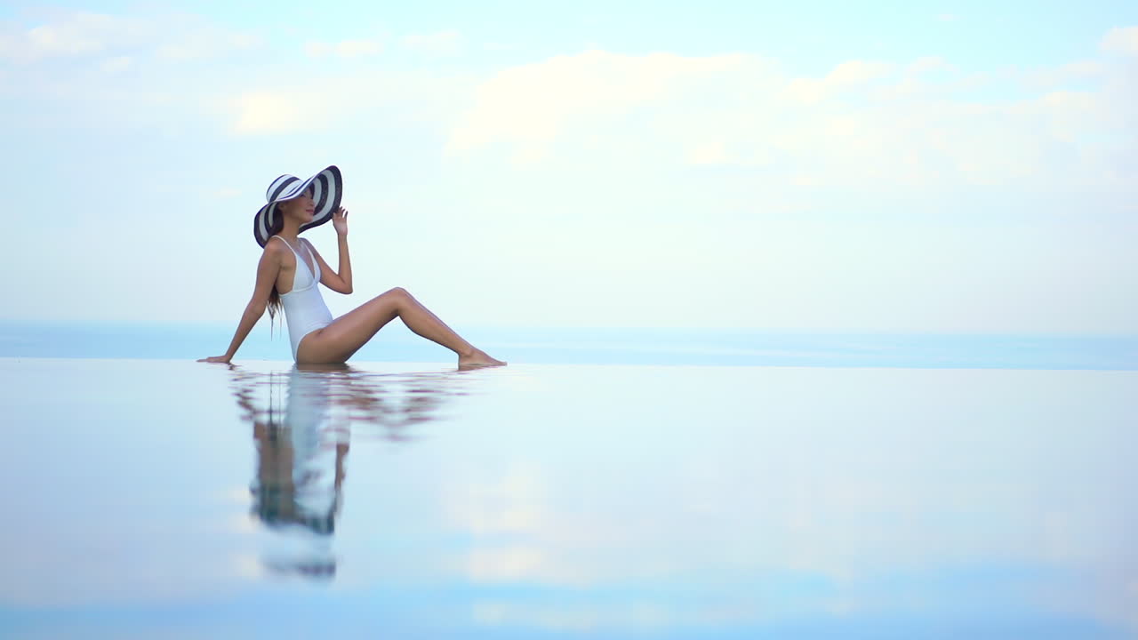 красивая молодая здоровая женщина сидит на краю бесконечного бассейна, создавая иллюзию, что она парит в воздухе