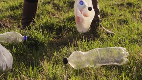 hand picking up empty water bottles and putting it inside bag, rubbish on grass park, cleaning environment, closeup day