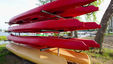 una pila de kayaks rojos almacenados en estantes metálicos a la orilla del lago, con árboles y agua visibles en el fondo