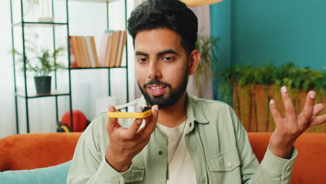 Happy-excited-Indian-man-making-phone-conversation-with-friends-sitting-call-on-couch-at-home-room