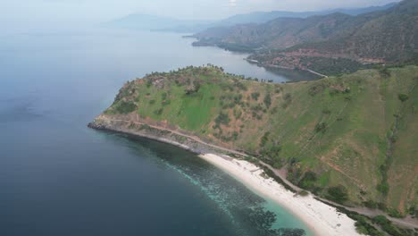 una costa pintoresca con aguas turquesas, una playa de arena blanca y colinas verdes, vista aérea