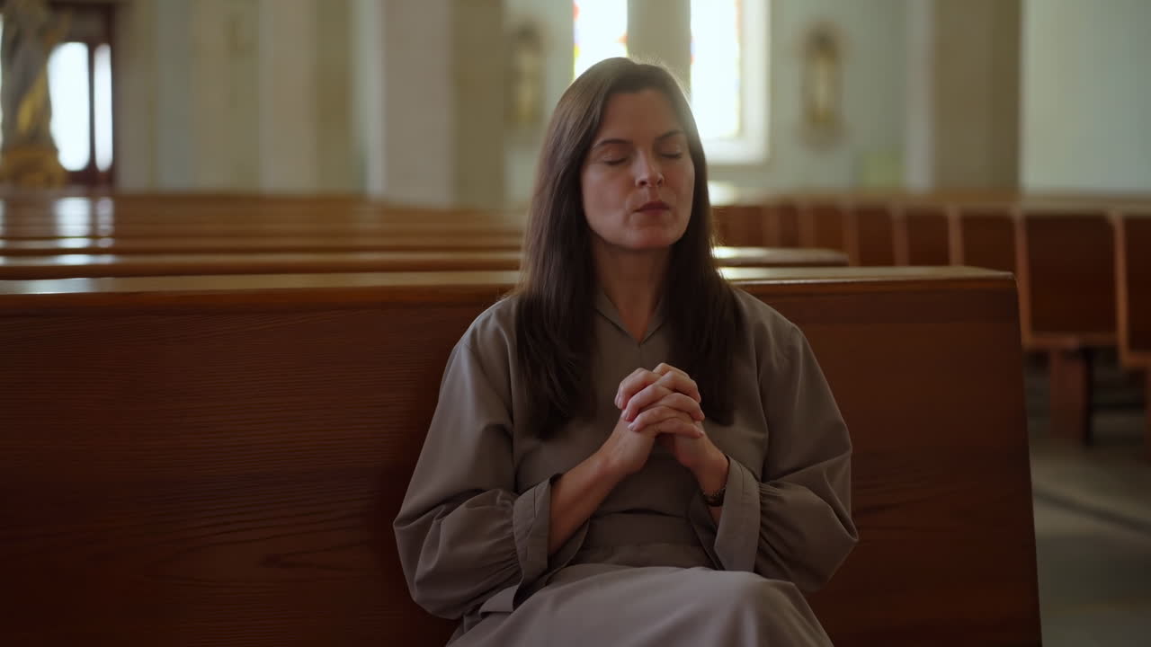 Mulher orando de olhos fechados no banco de uma igreja silenciosa