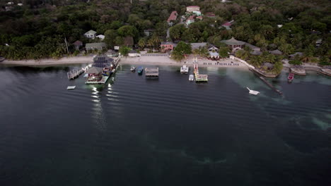aerial push-in over a popular bar on a dock near green trees on the beach shoreline in roatan, honduras