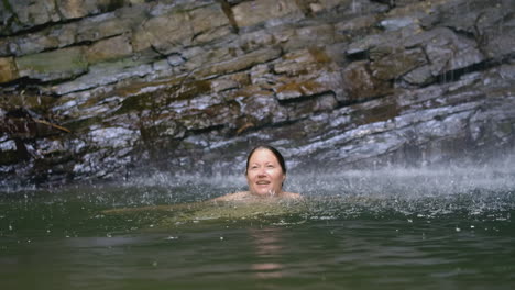 woman swimming under a waterfall