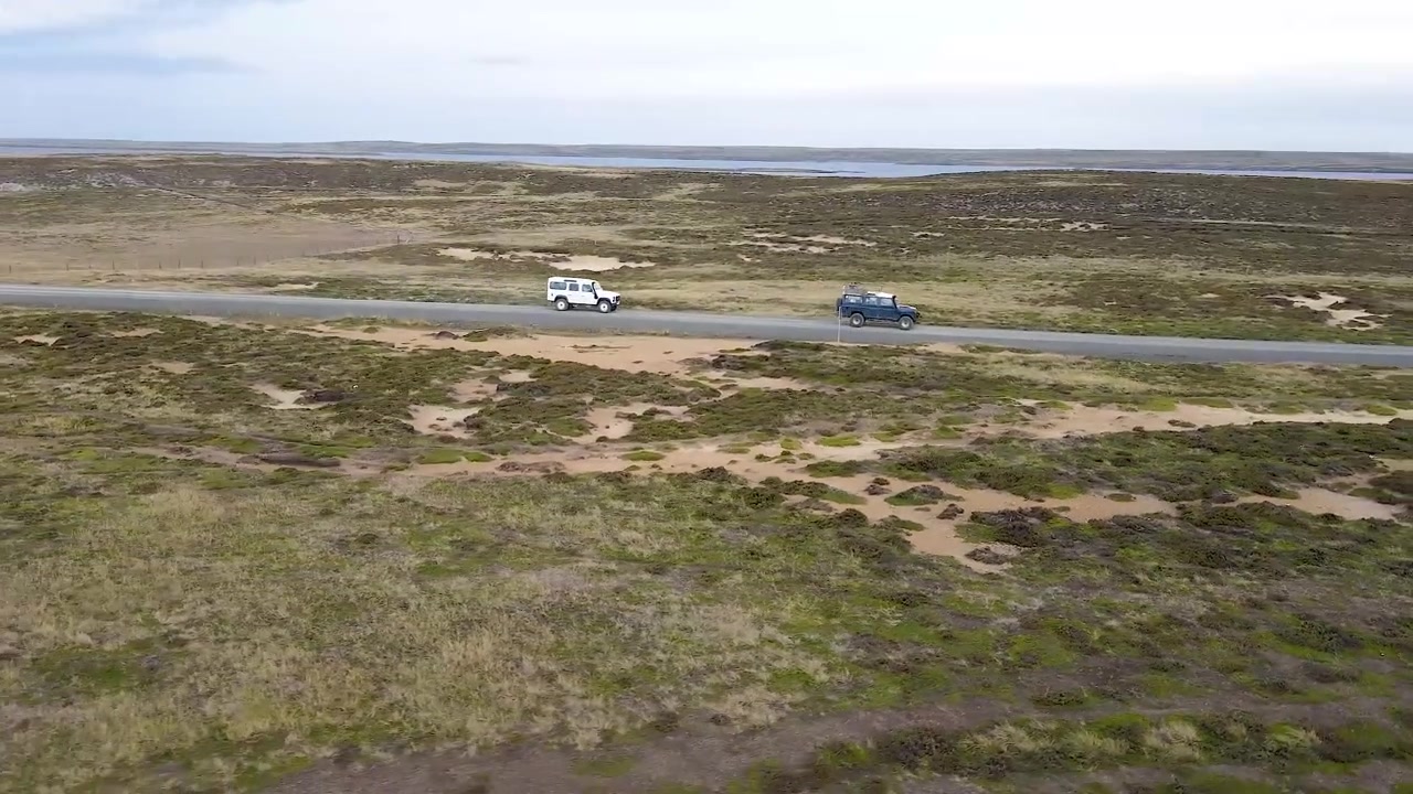 Dos coches llenos de turistas conducen a través de una puerta para entrar en una propiedad de rancho privado en un día soleado de verano.