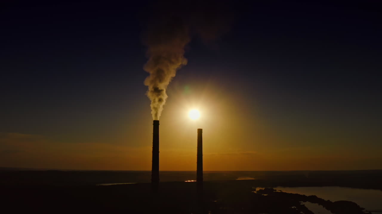 Smoke from manufacturing at darkness. Industrial pipes with chemical emissions on the setting sun background. Pollution the environment.