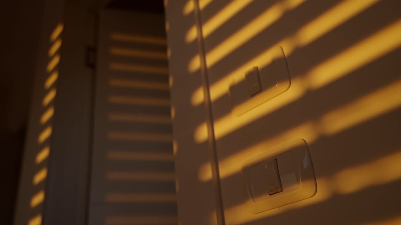 Shadow on a wall of electric or mechanical window opening or rolling up in house or apartment. Early morning orange warm light or sunset afternoon sunlight shining through horizontal cracks