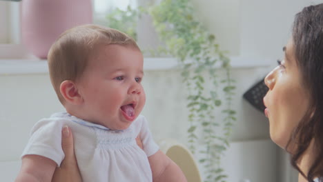 close up of loving mother playing with baby son at home at kitchen counter