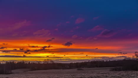 Timelapse-of-clouds-moving-in-colorful-sky-with-rising-sun-at-horizon-over-snowy-landscape-at-sunrise