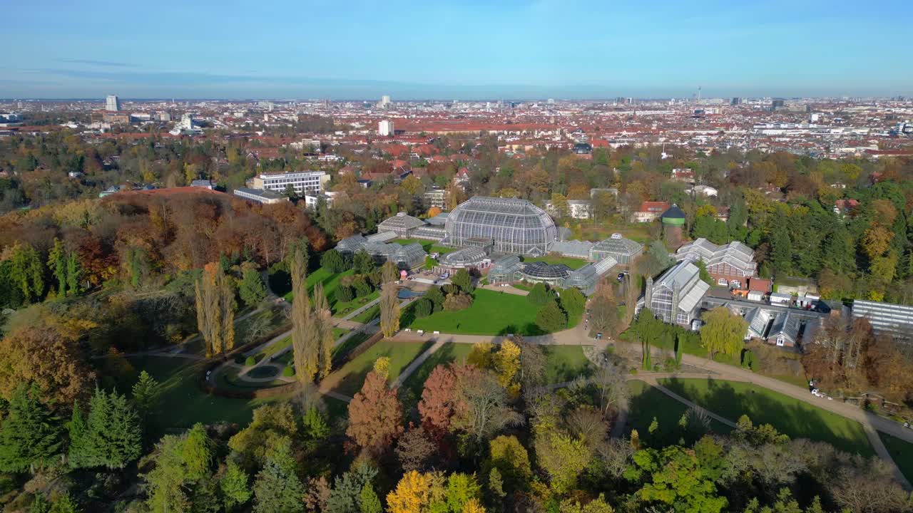 Botanical Garden Berlin 100-year old Victoria House greenhouses surrounded by autumn trees and urban landscape. Fantastic aerial view flight descending drone