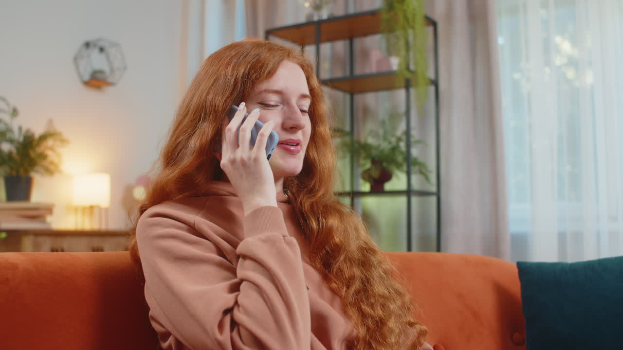 Smiling young caucasian woman making phone conversation with friends sitting on sofa couch at home