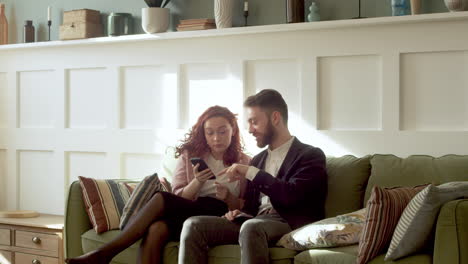 woman and man in formal wear using mobile phone and talking together while sitting on sofa 3