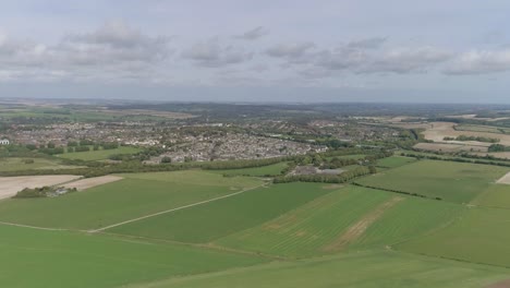 Wide-aerial-tracking-forward-toward-the-town-of-Poundbury,-just-outside-of-Dorchester,-Summer-weather,-fields-are-vibrant