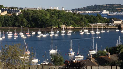 a small boat travels down the river tamar between devon and cornwall with many yachts on either side between devon and cornwall