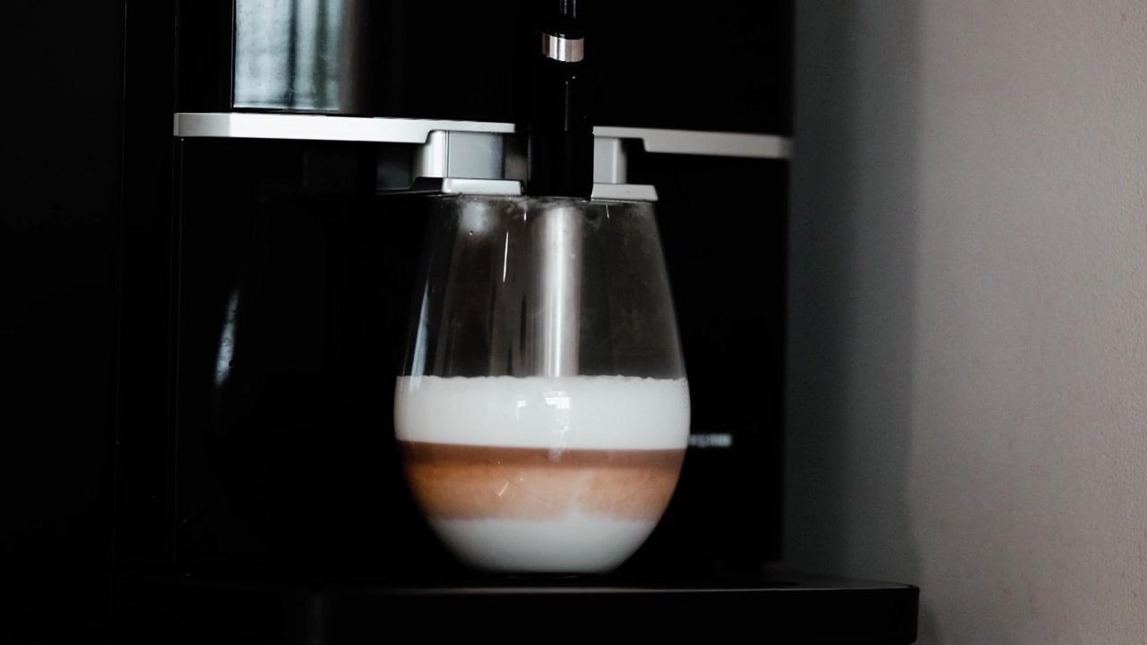 A coffee machine drips a shot of espresso into a glass of frothy milk