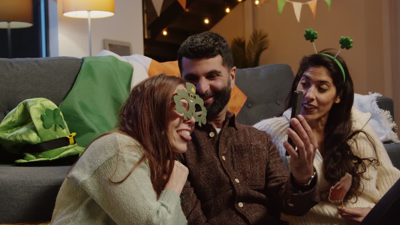 Amici che si travestono con gadget e accessori irlandesi a casa, in posa per un selfie, festeggiando a una festa di San Patrizio 3.