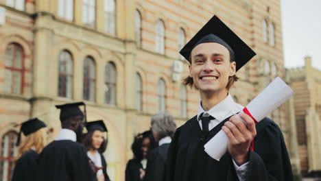 Retrato-Del-Joven-Graduado-Caucásico-Feliz-Posando-Para-La-Cámara-Y-Mostrando-Su-Diploma-Frente-A-La-Universidad