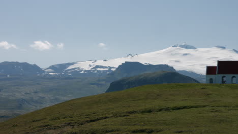 ingjaldshólskirkja church on green hill, snowy glacier in background, pan right