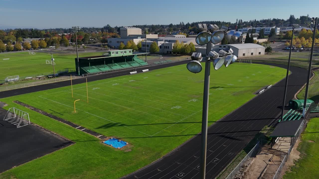 Drone pass by light tower at a high school football field with a lone woman on the track