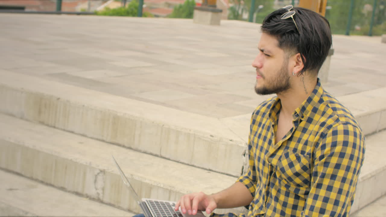 Hombre apuesto sentado en escaleras usando laptop al aire libre