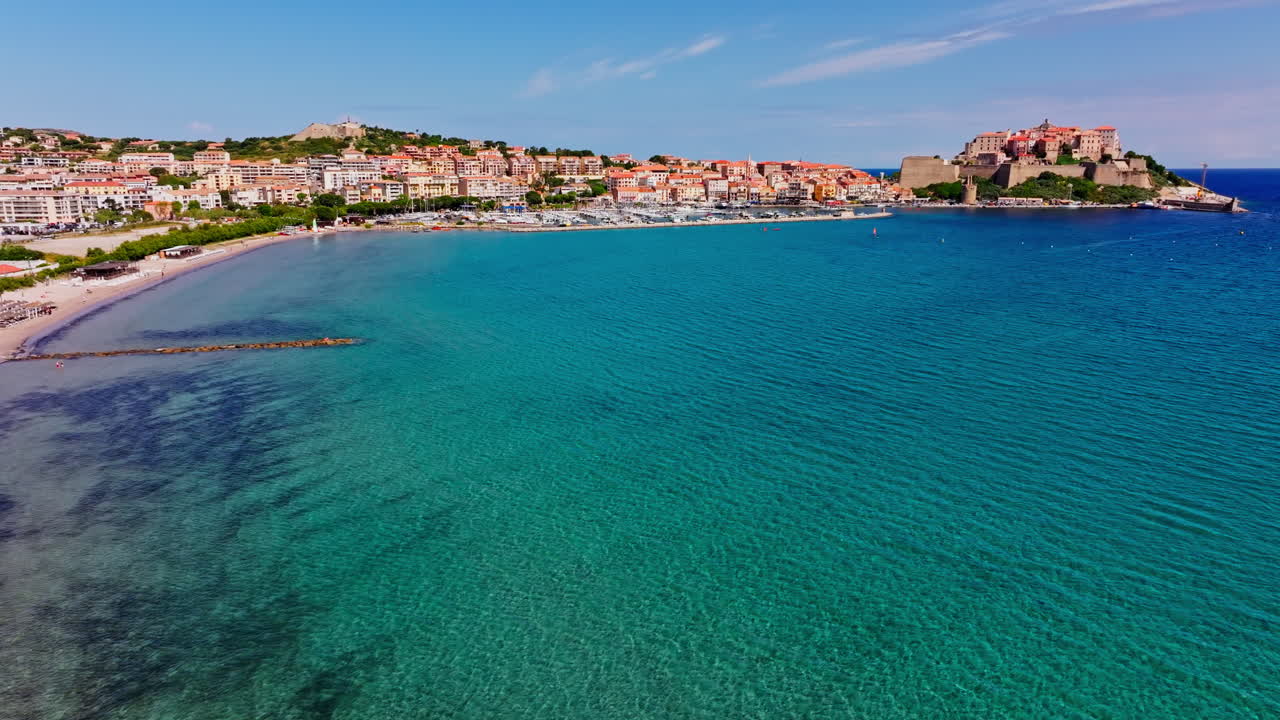 Ripresa aerea con drone sulla città costiera di Calvi, in Corsica. Vista della cittadella che domina la città. Destinazione per le vacanze estive. Cielo blu, mare turchese brillante, spiaggia lunga e ampia.