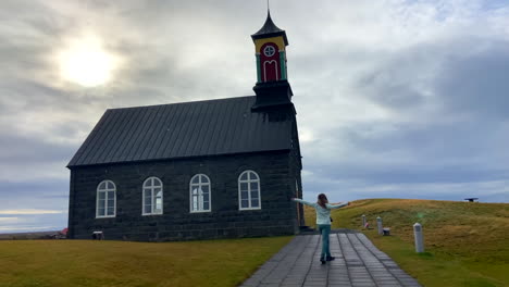 Cheerful-caucasian-female-tourist-enjoying-the-snow-outside-an-Icelandic-Hvalsnes-church