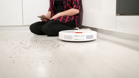 Woman with smartphone controls robot vacuum cleaner at home