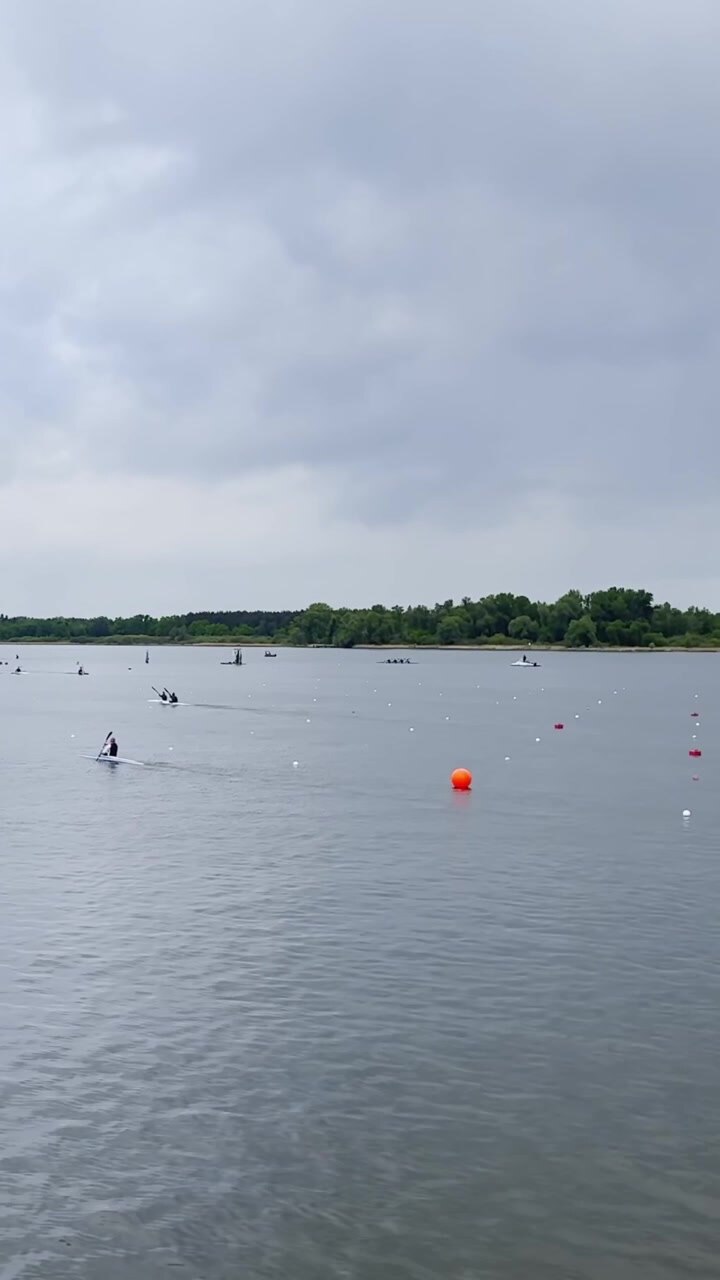 Canoe sprint athletes paddle across marked racing lanes on Beetzsee in Brandenburg, vertical static