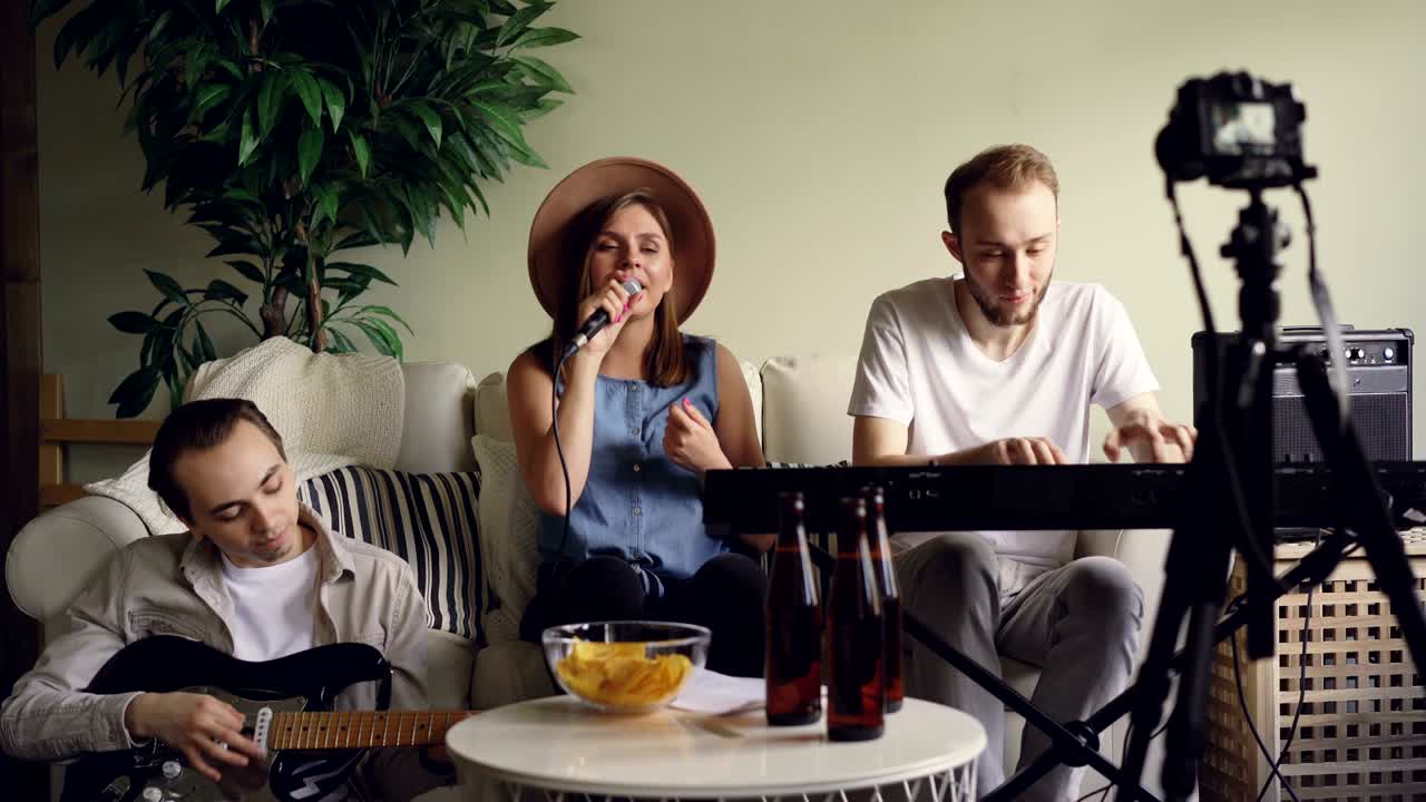 los alegres miembros de la banda están grabando un video de su práctica para un blog en línea, están cantando y tocando instrumentos musicales mirando a la cámara en un trípode.