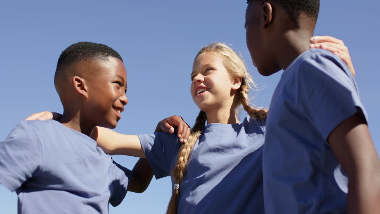 Three preteen teammates huddling, center girl placing arms, giving pep talk on field in blue shirts