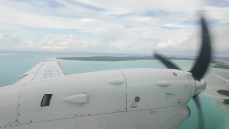 raindrops on window, inside airplane looking out at wing and propellor over tropical atoll islands