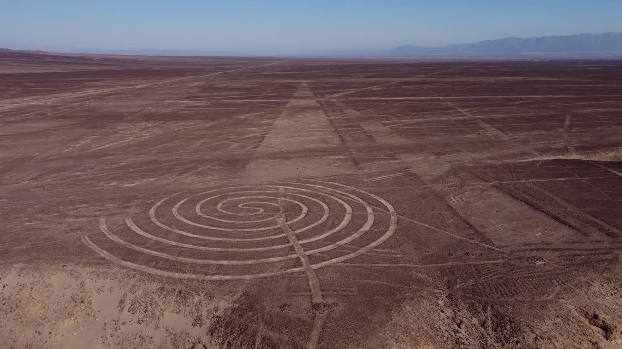 Spiral and long linear ancient geoglyphs drawn on flat desert plateau. Part of the world famous Nazca Lines. Drone flies forward tilting camera up to the horizon. Located in Nazca, Peru