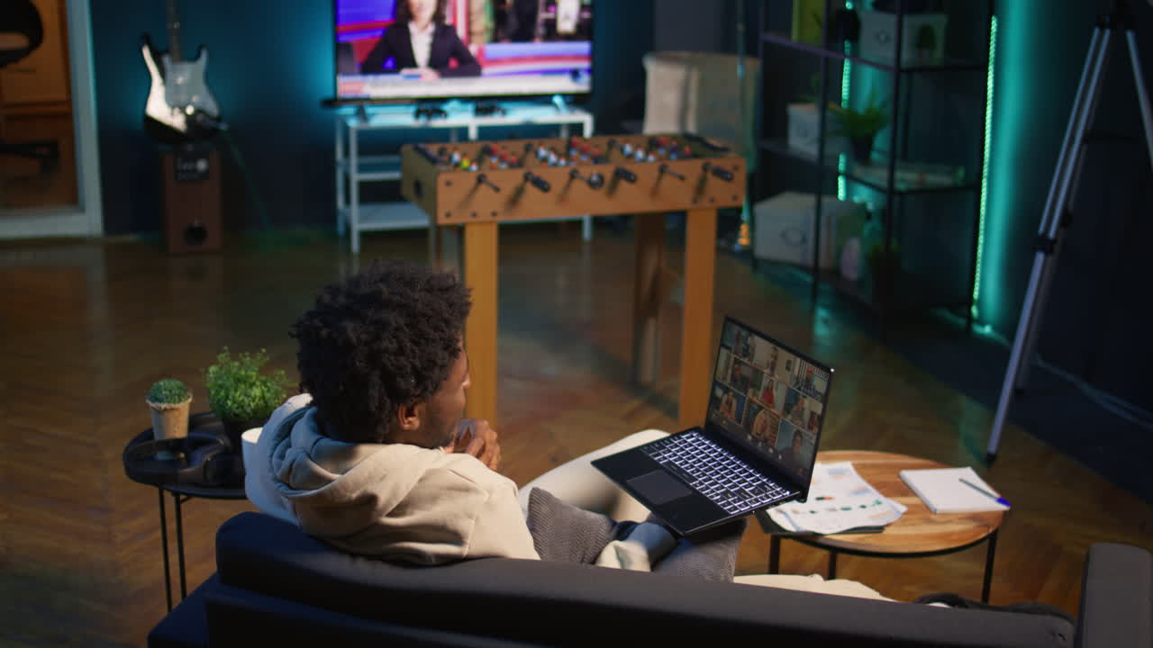 Confident male speaker greeting colleagues on a video conference meeting, enjoying benefits of online remote communication in cozy loft. Young black adult hosting virtual discussion. Camera B.