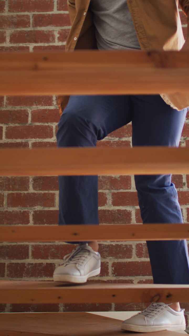 video vertical de la sección baja de un hombre afroamericano subiendo una escalera de madera