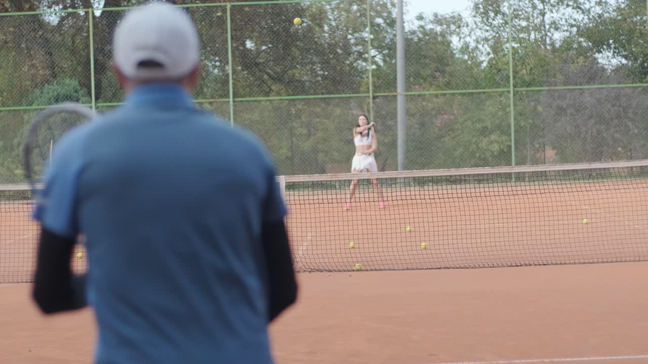 A young woman practicing tennis on an outdoor court with a coach. The coach provides guidance as the player works on her technique, perfecting her strokes in an athletic training session.