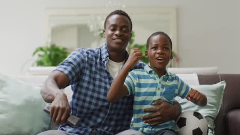 happy african american father and son cheering while watching match in tv