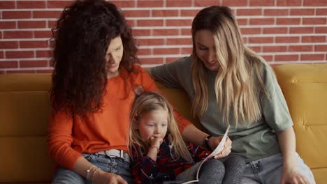 close up of young women read a book together to a small preschool girl on sofa