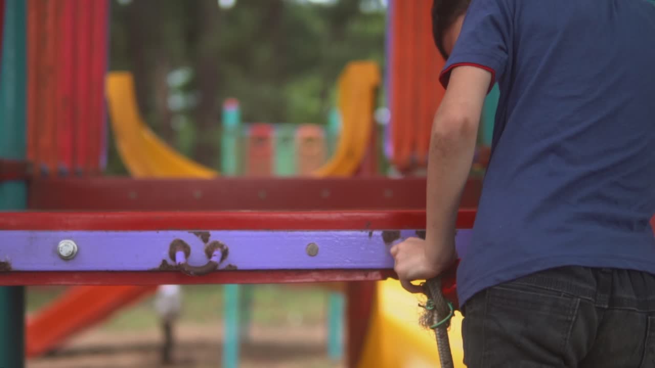 Slowmotion static shot of a kid in a blue shirt in a playground