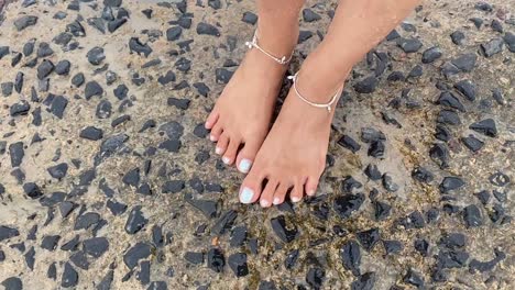 waves hitting the legs of an indian girl standing in a stone in a beach