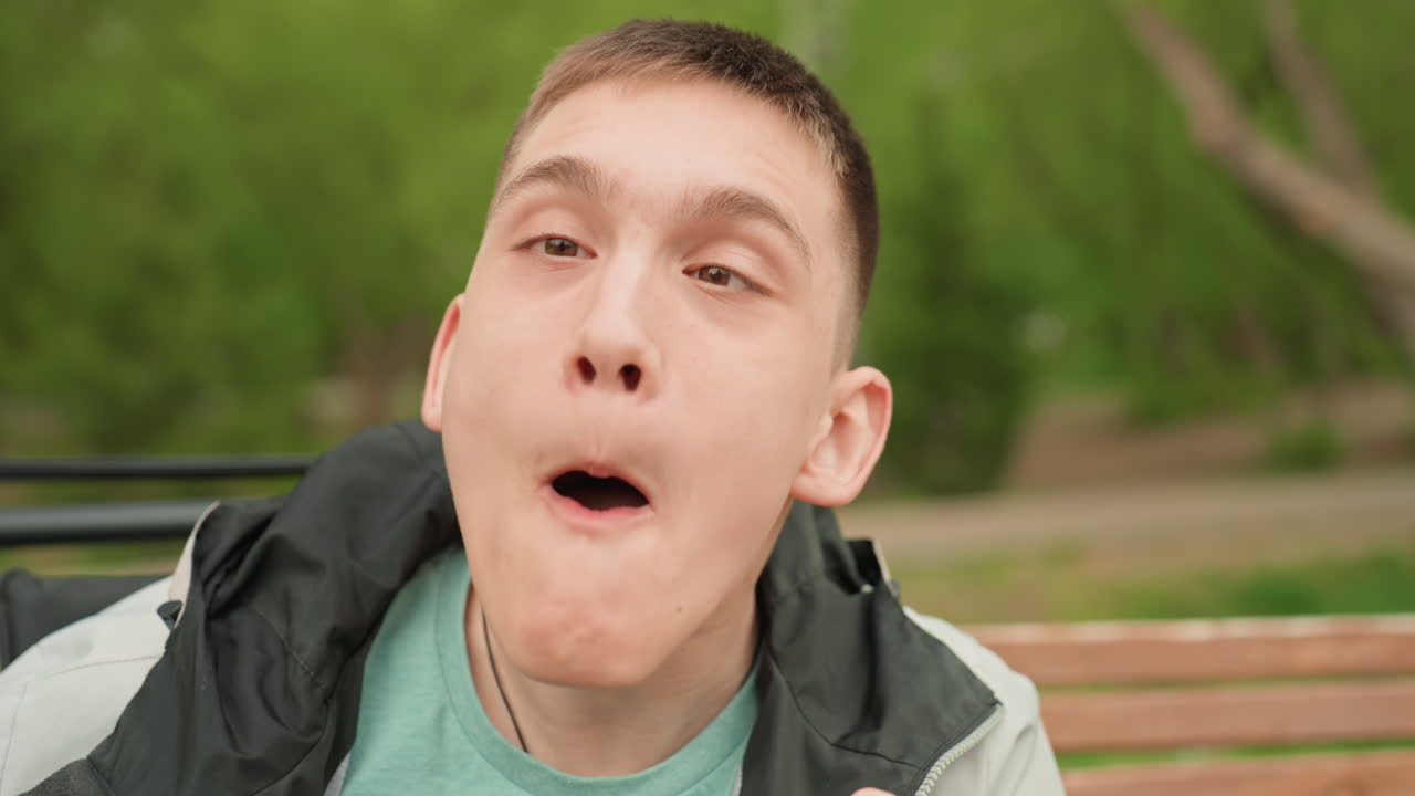 Man In Wheelchair Showing Amusing Face Poses, Carefree Individual Seated On Bench Making Exaggerated Funny Faces, Joyful Young Man Seated On Park Bench Humorously Contorting His Face And Eyes