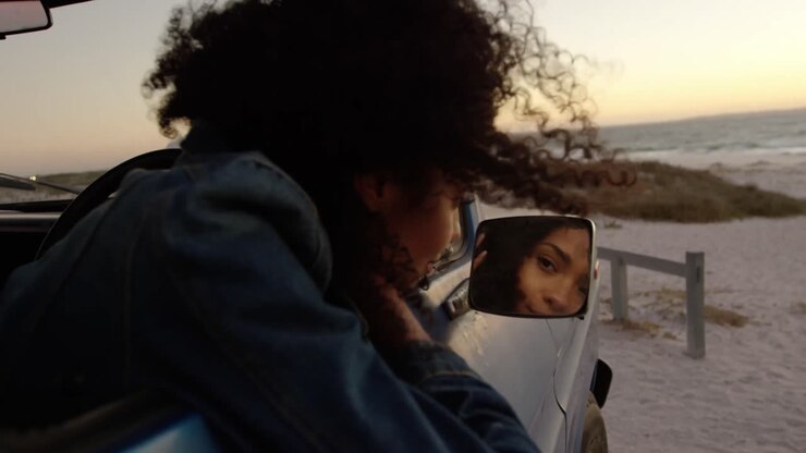 Woman looking in wing mirror of pickup truck at beach 4k