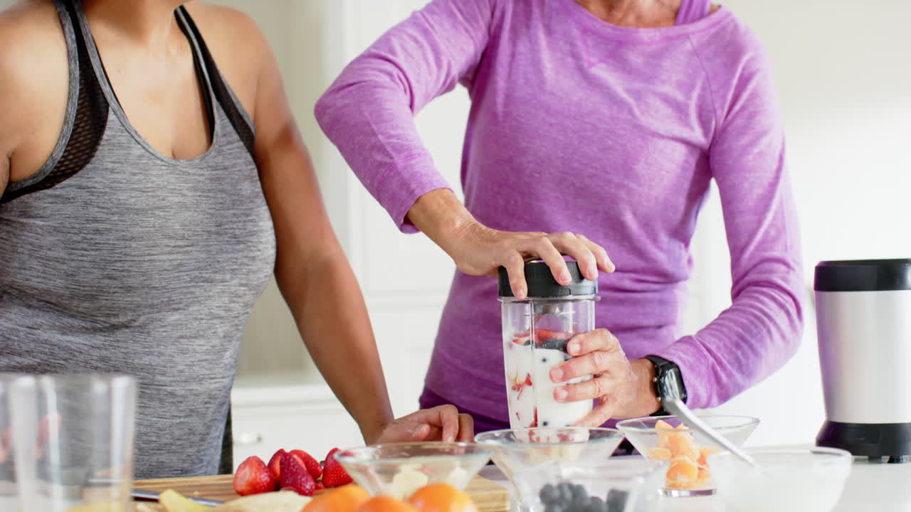 dos mujeres mayores felices y diversas preparando cócteles y discutiendo en la cocina, en cámara lenta