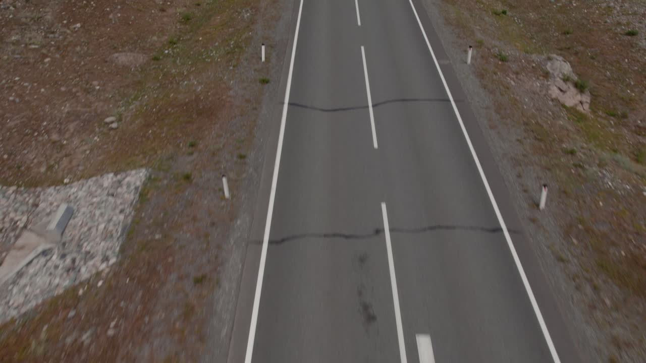 Drohnenaufnahme der leeren Tschujatrakt-Straße, die sich durch raues Altai-Gelände in Russland schlängelt, Draufsicht mit Fahrbahnmarkierungen, abgelegene Reiseroute und Wildnislandschaft.