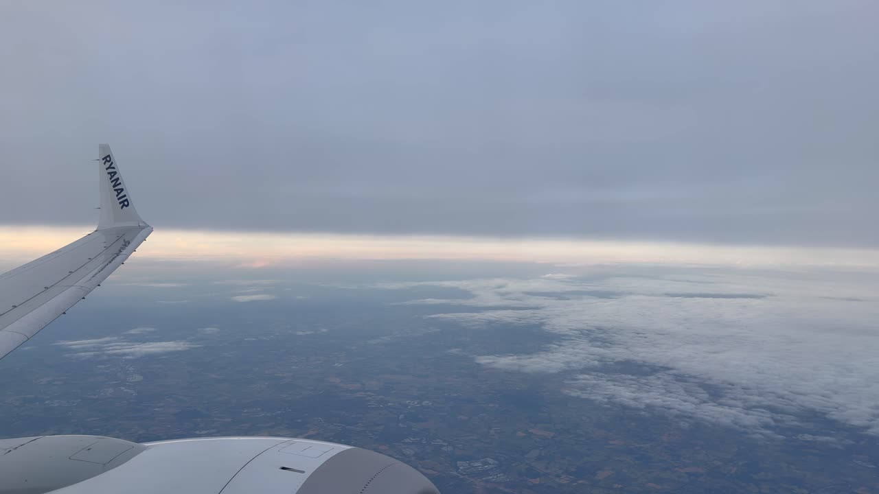 View of an airplane wing over fluffy clouds during a scenic flight at sunrise