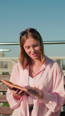 estudiantes masculinos y femeninos estudian al aire libre en un banco; él escribe en una computadora portátil, ella lee de un libro, ambos involucrados en una actividad de aprendizaje, el horizonte urbano en el fondo bajo el cielo azul