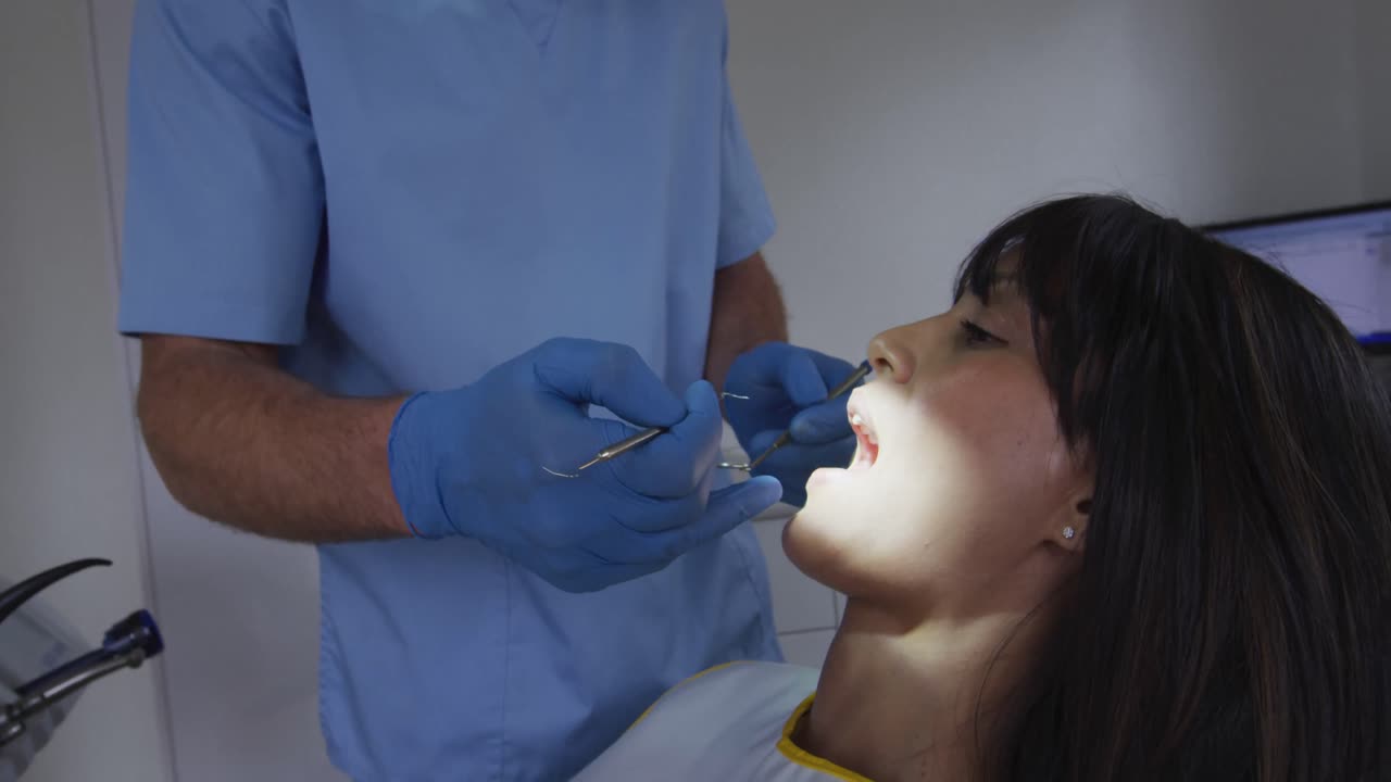 Dentista masculino caucasiano examinando os dentes de uma paciente em uma clínica odontológica moderna.