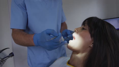 dentista caucásico examinando los dientes de una paciente en una clínica dental moderna