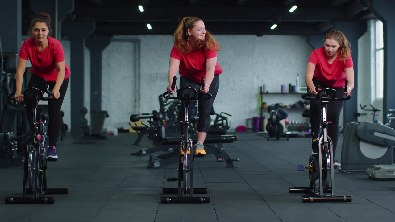 Gruppo di ragazze atletiche che eseguono esercizi di allenamento aerobico su una bicicletta stazionaria in palestra