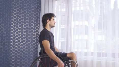 unhappy disabled man looking out the window, feeling sad and helpless at home.