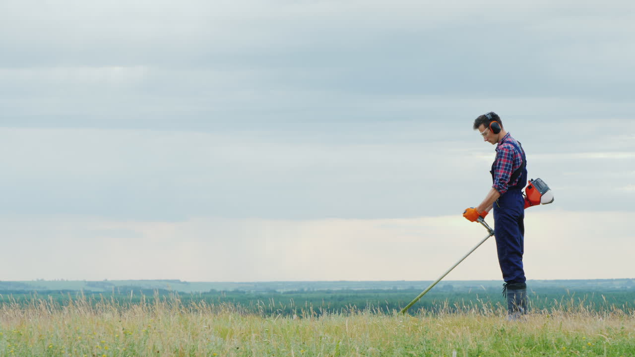 그림 같은 초원에서 트리머로 잔디를 깎고 있는 청년